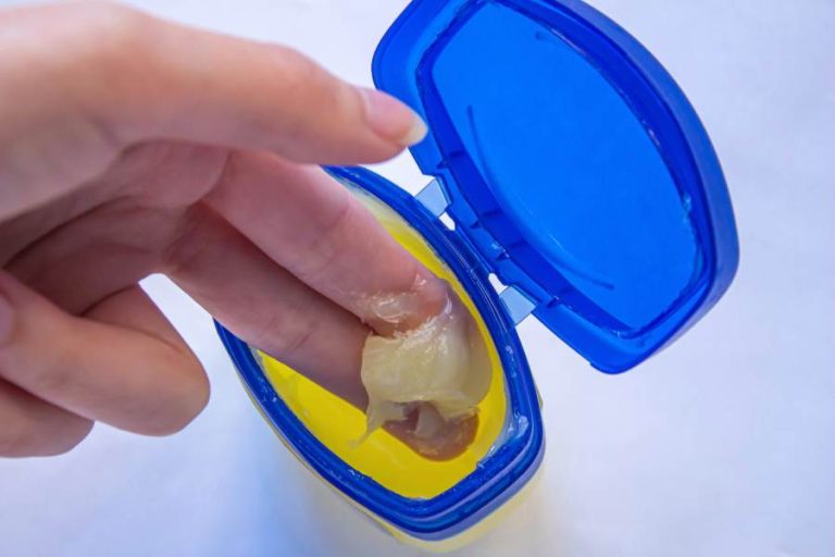An opened pot of vaseline with two fingers scooping some out